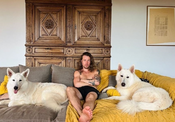 Julien Doré et ses deux chiens Berger Blanc Suisse Simone et Jean-Marc, tous les 3 assis sur le canapé